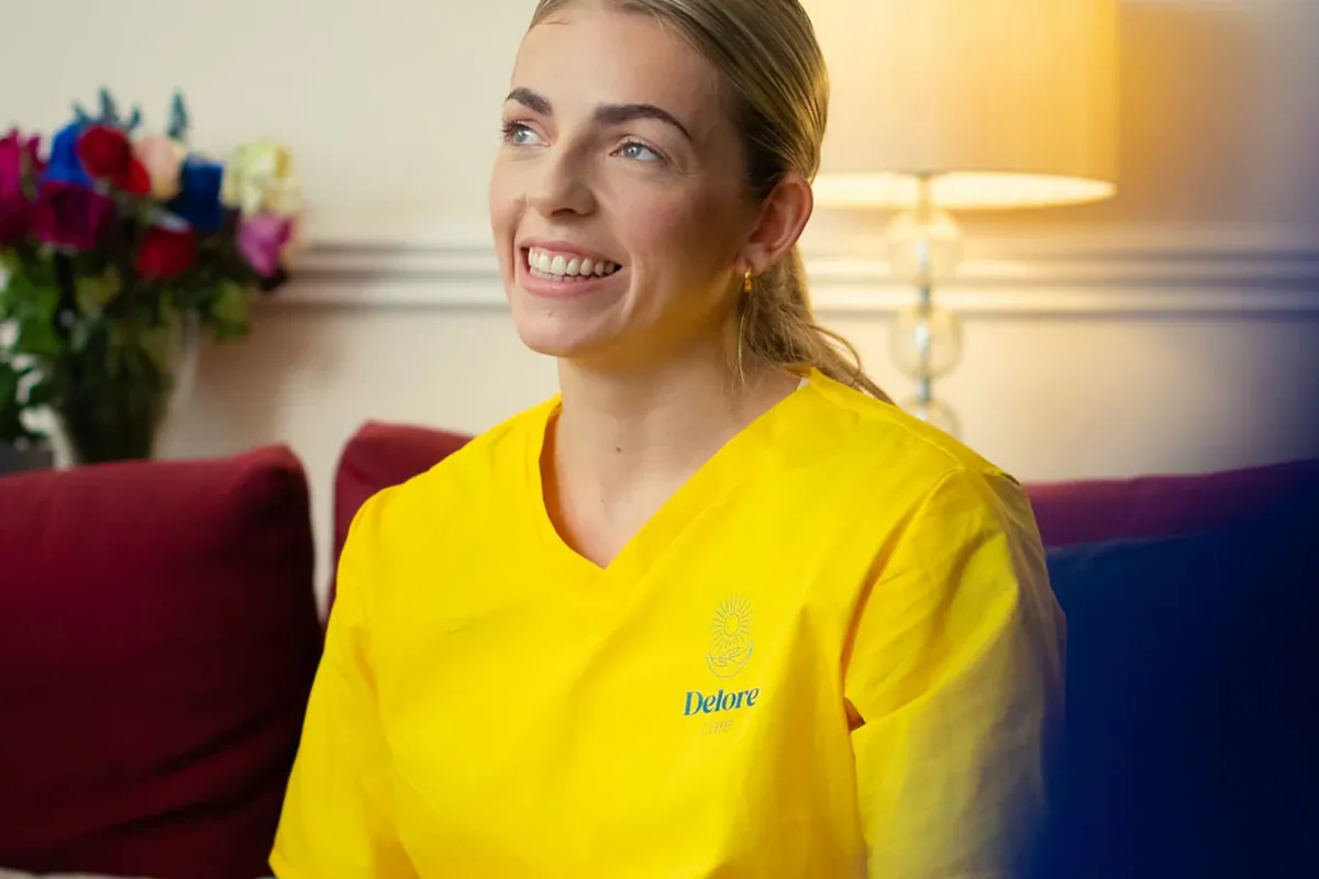 Smiling woman in a yellow care uniform indoors.